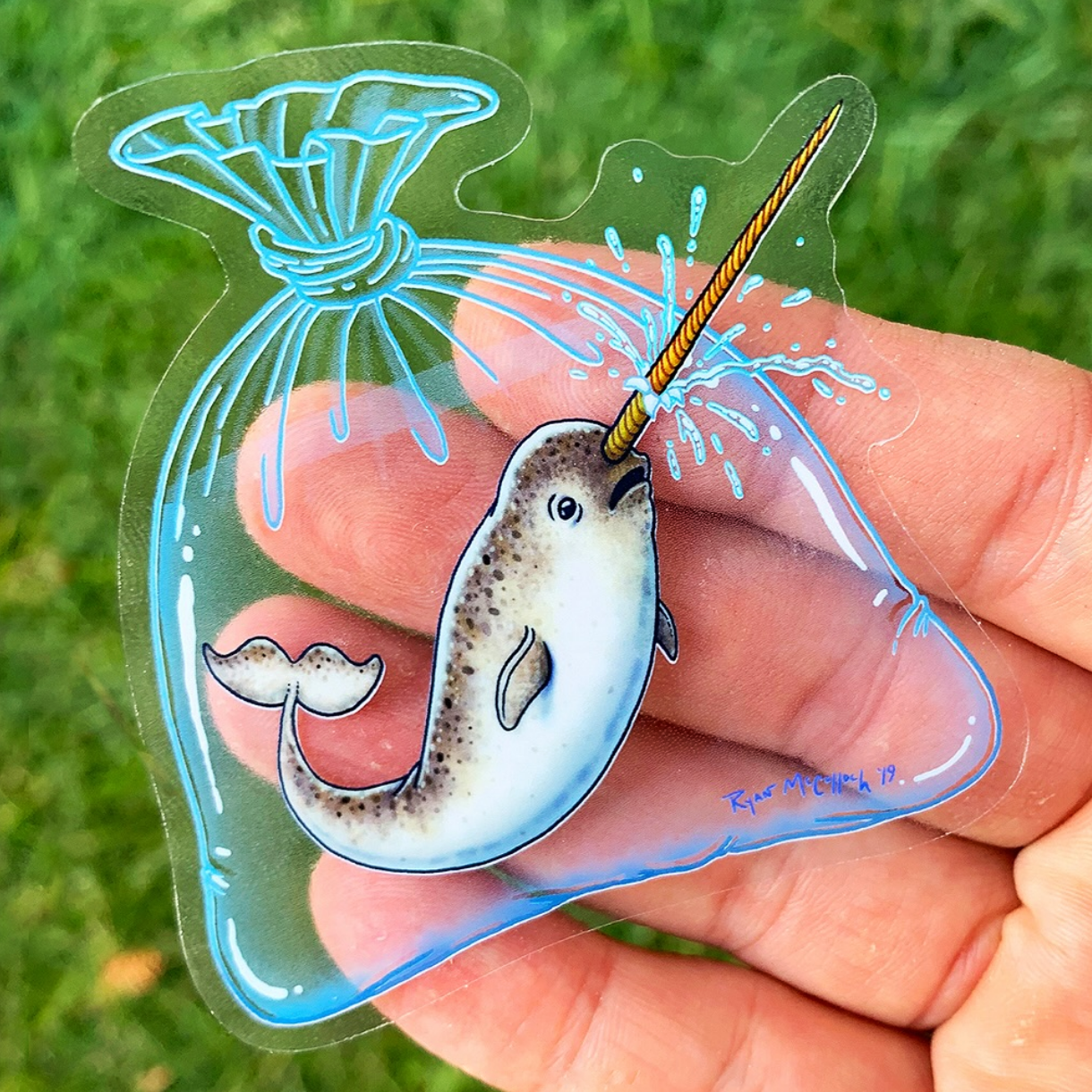 Die-cut transparent sticker showing a narwal captured and poking a hole in a plastic bag, against a grassy background