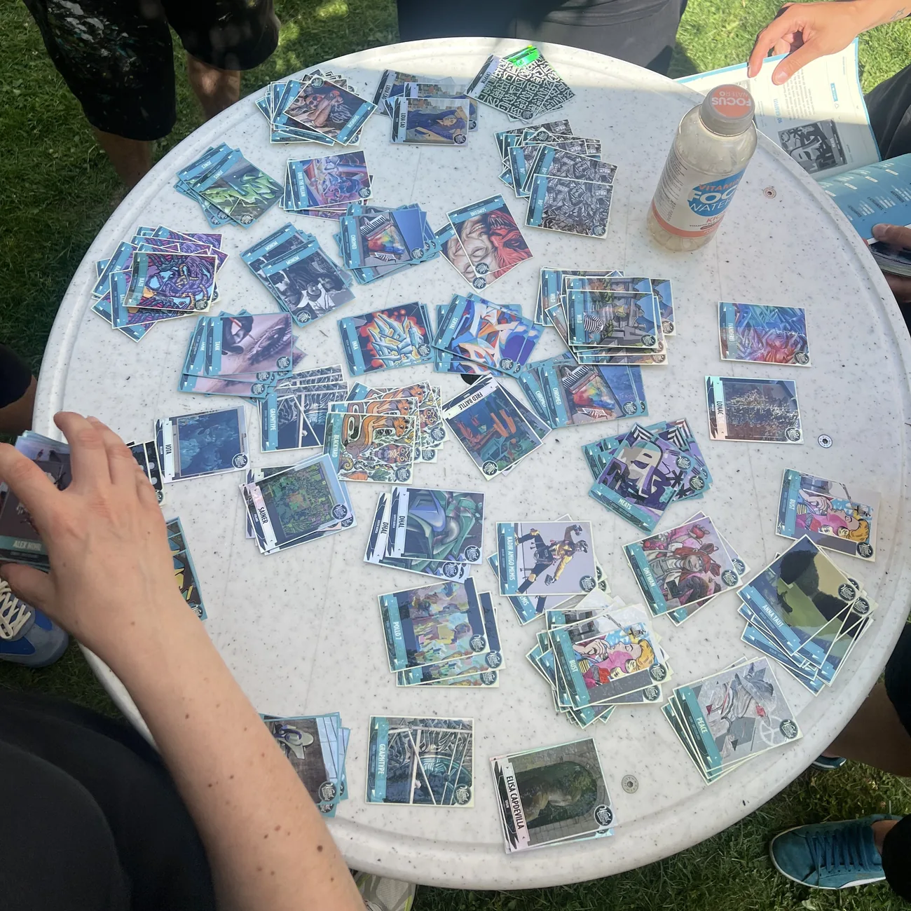Asistentes al festival completan álbumes azules con cromos adhesivos de arte urbano repartidos sobre una mesa redonda