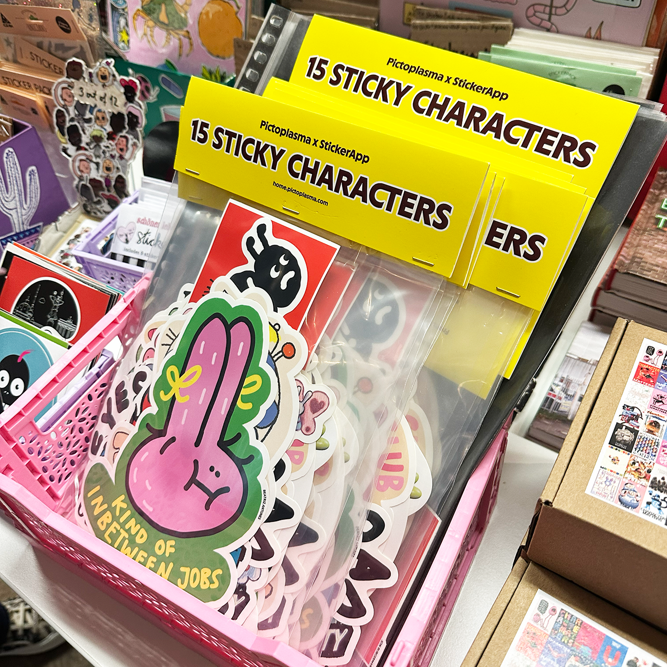 Sticker packs with different die-cut stickers, displayed with other stickers and merch, at a trade show.