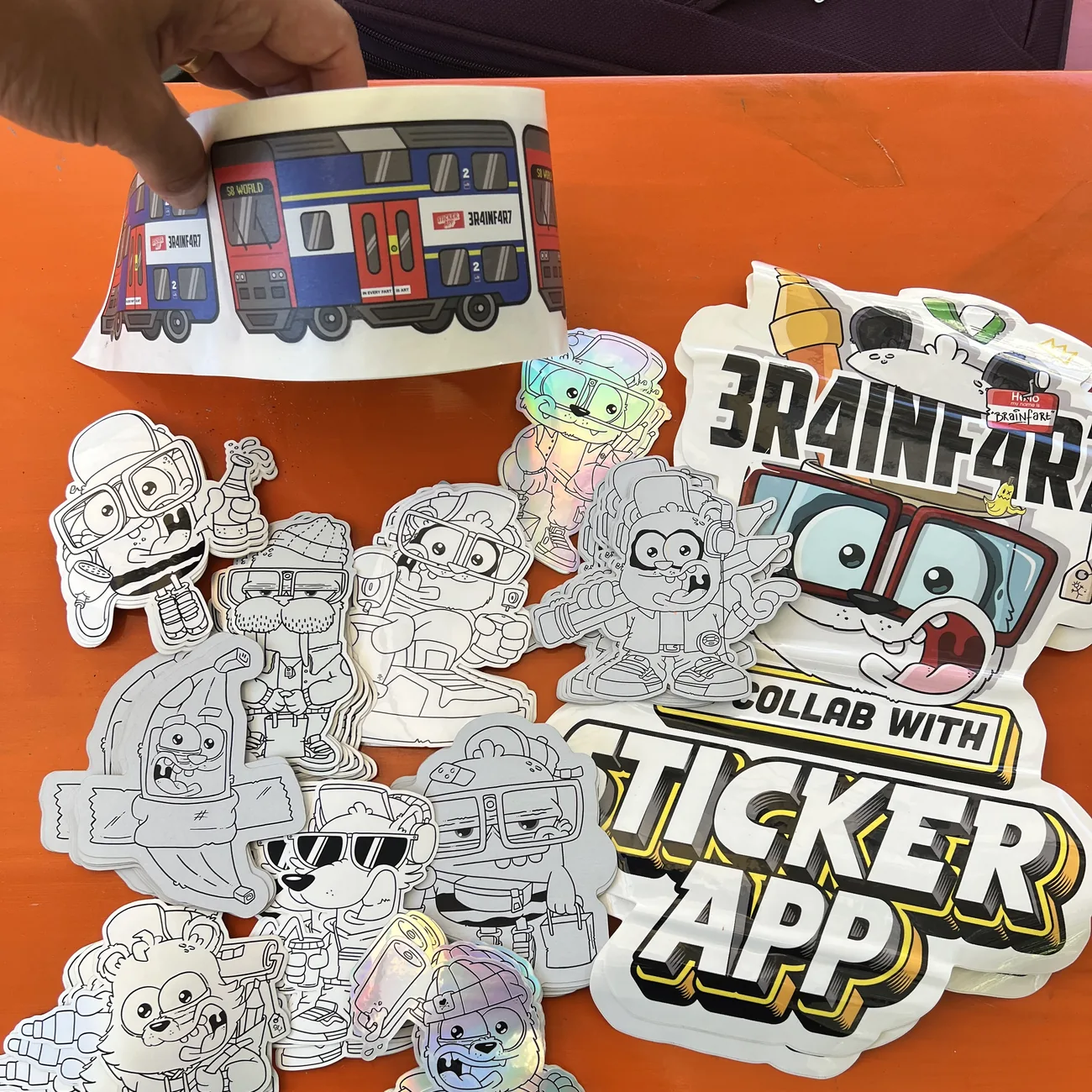 Etiqueta del tren S8 World de Brainfart x StickerApp con el cartel "In every fart is art", sostenida sobre pegatinas troqueladas en blanco y negro