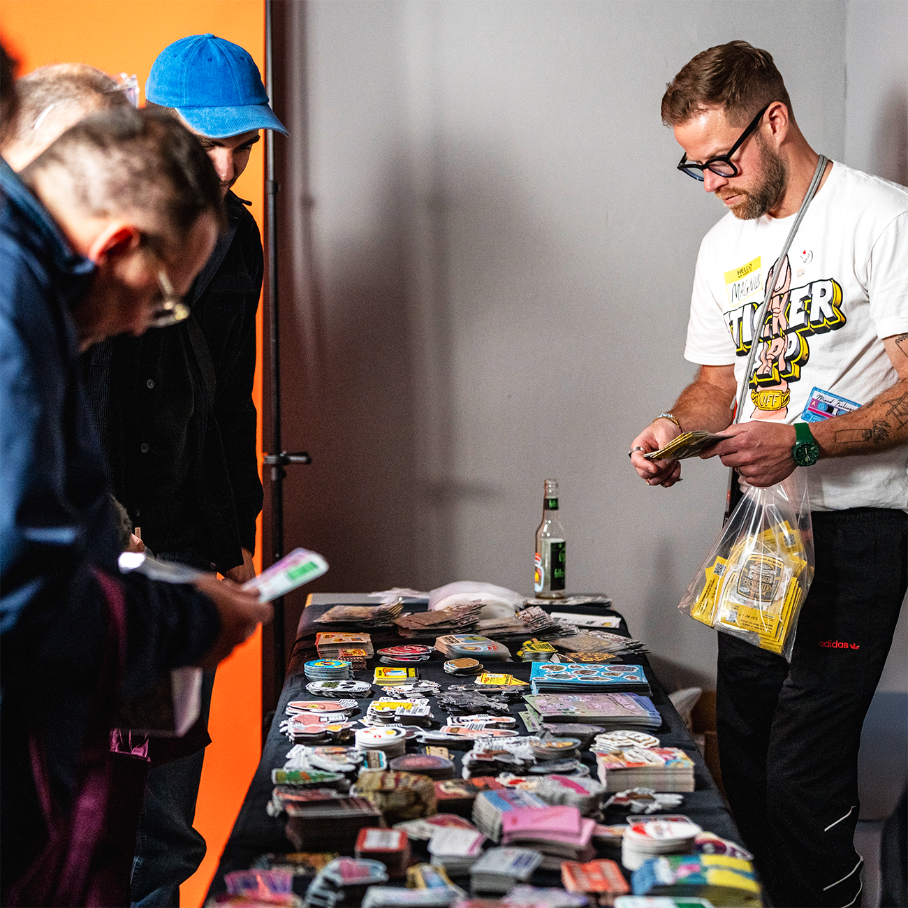 Visitors at a booth at an exihibtion, looking at ant grabbing various die-cut stickers laying on a table with a salesperson behind.