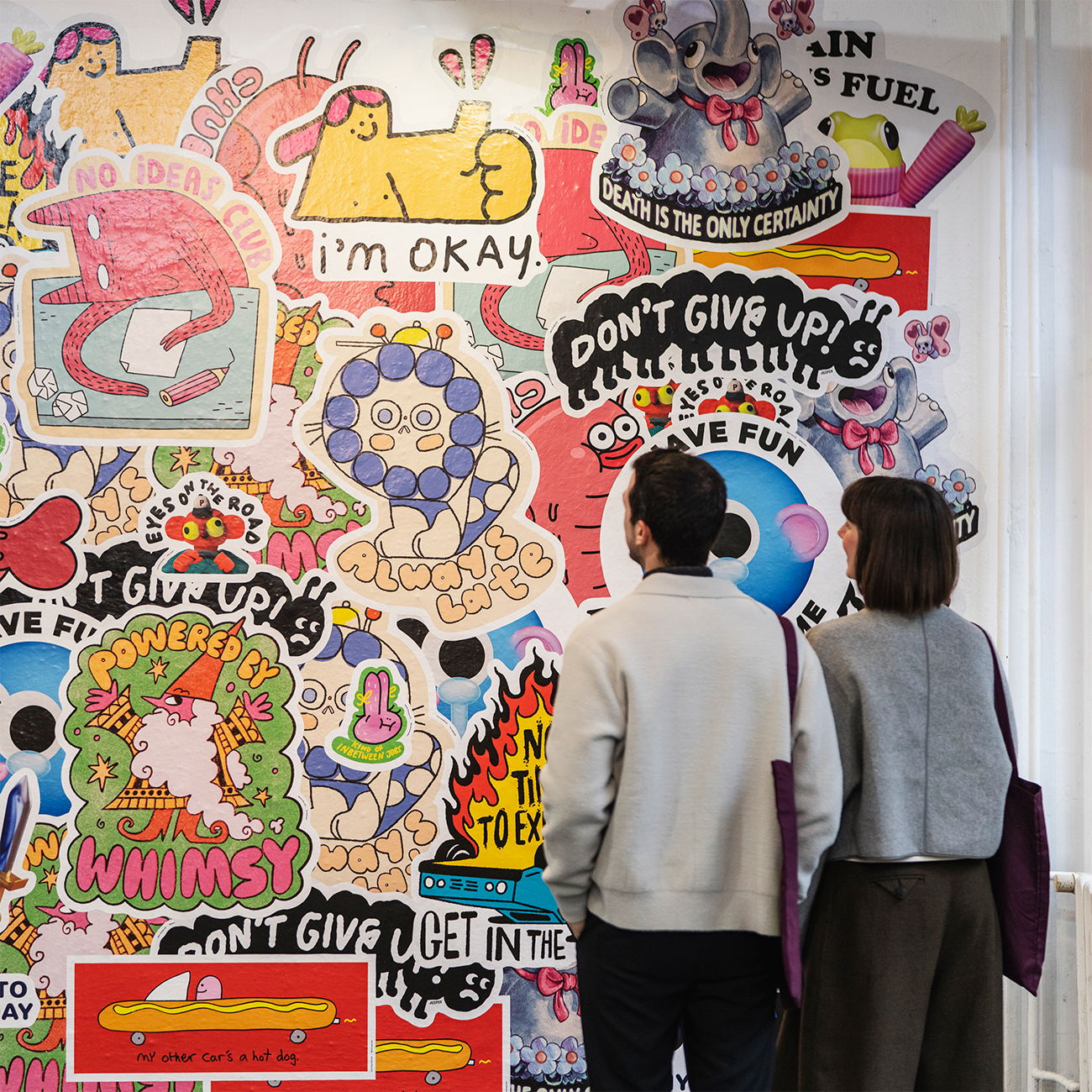 Two people standing in front of a wall covered in wall stickers in various shapes and sizes.