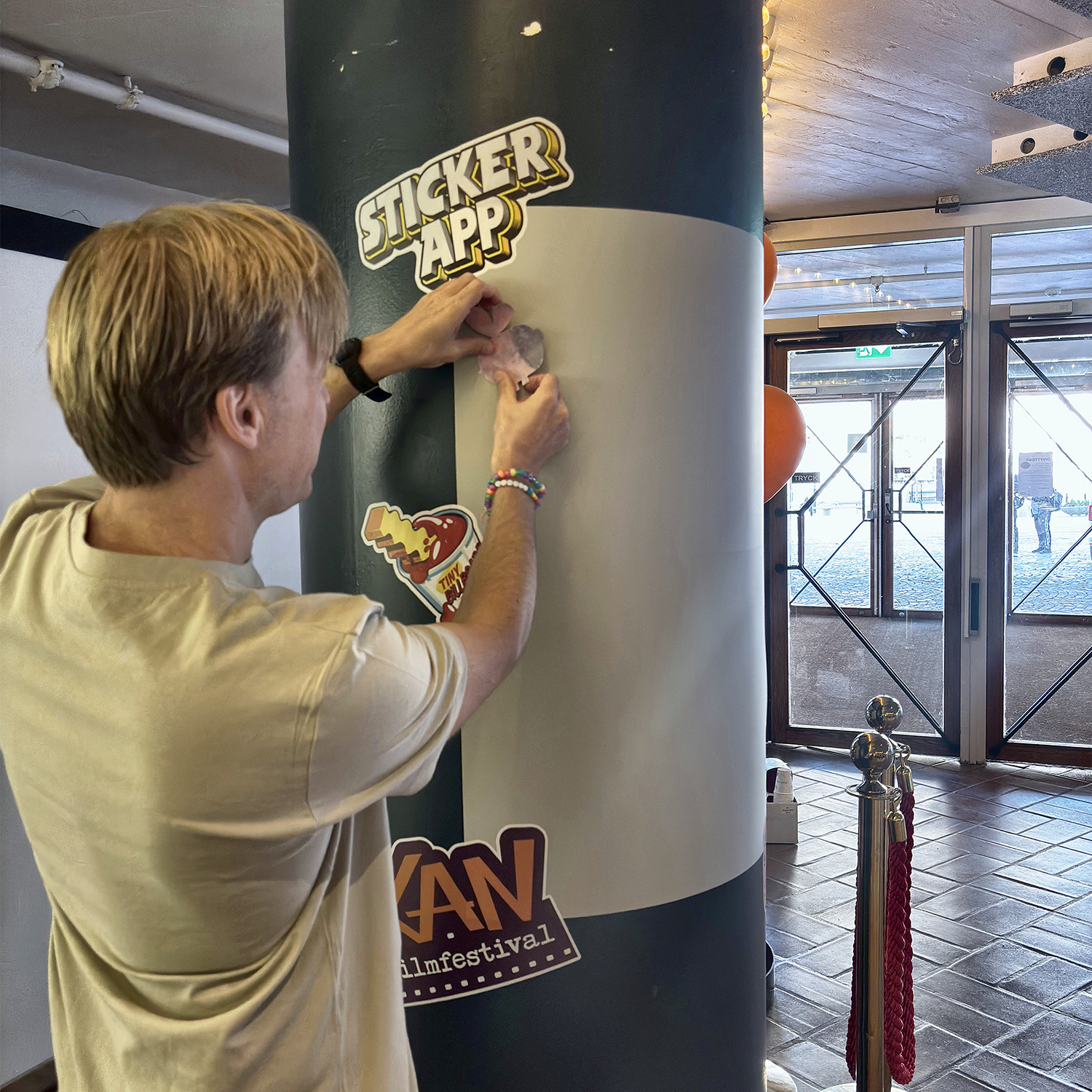Hombre pegando una pegatina en un muro de pegatinas de StickerApp que rodea una columna en el KAN Film Festival