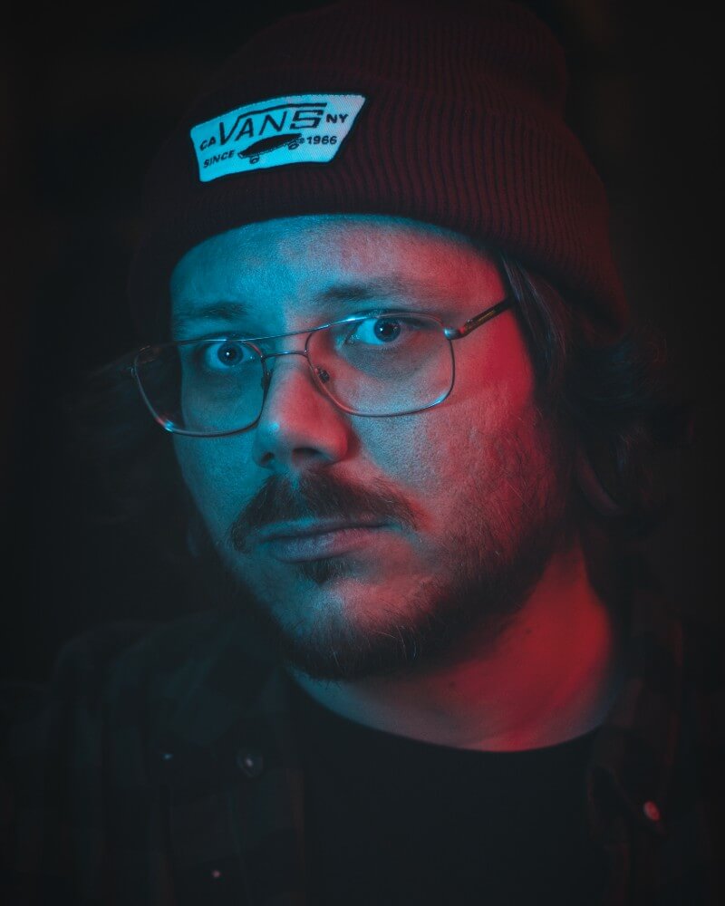 Retrato del artista Emil Ronnelin (Bloodstrokes) con gafas y gorro bajo luz roja y azul